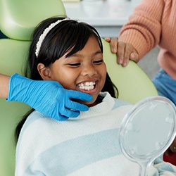 Girl looking at her teeth in the mirror while in the treatment chair