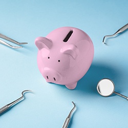 A piggy bank surrounded by dental tools against a blue background