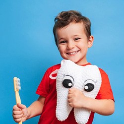 Child holding a toothbrush and plushie of a tooth