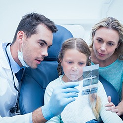 Dentist reviewing X-rays with child and mother